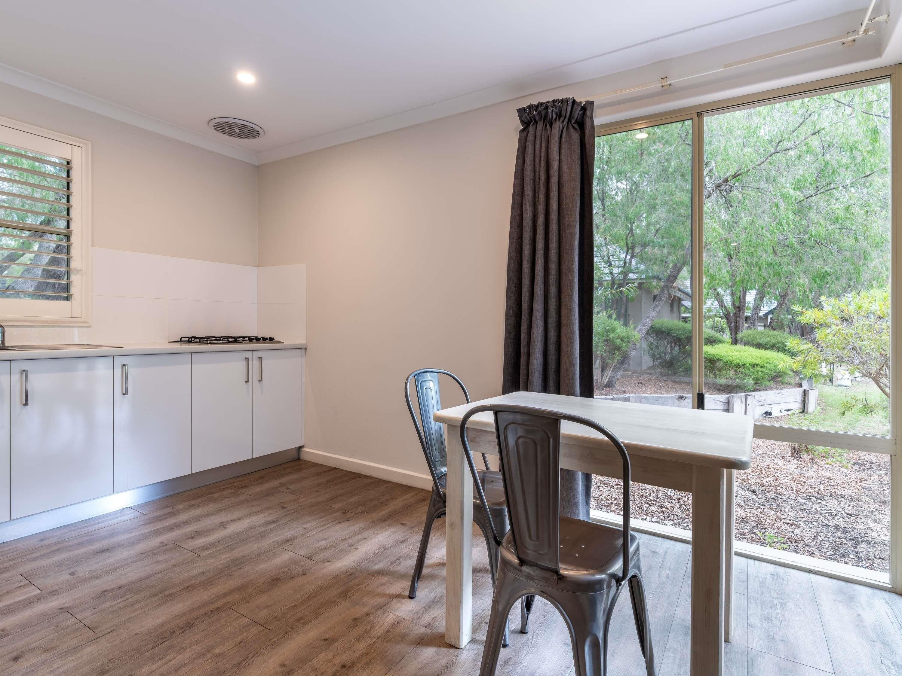 A modern kitchen with white cabinets, a wooden floor, and a window with a view of greenery.