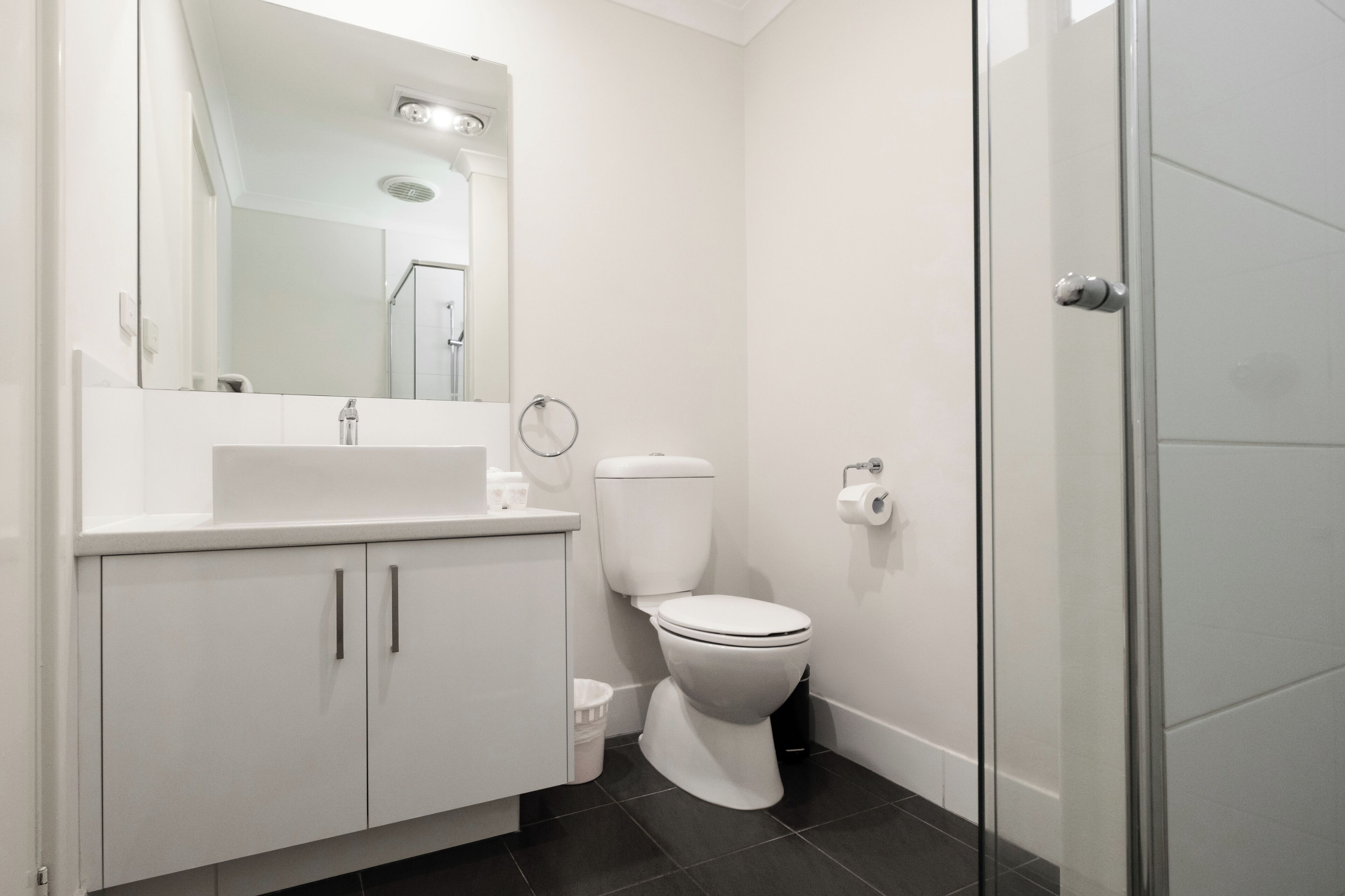 Ein modernes Badezimmer mit Waschbecken, Spiegel und Toilette in Weiß.