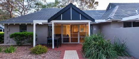 A modern house with a covered patio, a brick pathway, and a well-maintained garden.