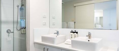A modern bathroom with a glass shower enclosure, two sinks, a large mirror, and white cabinetry.