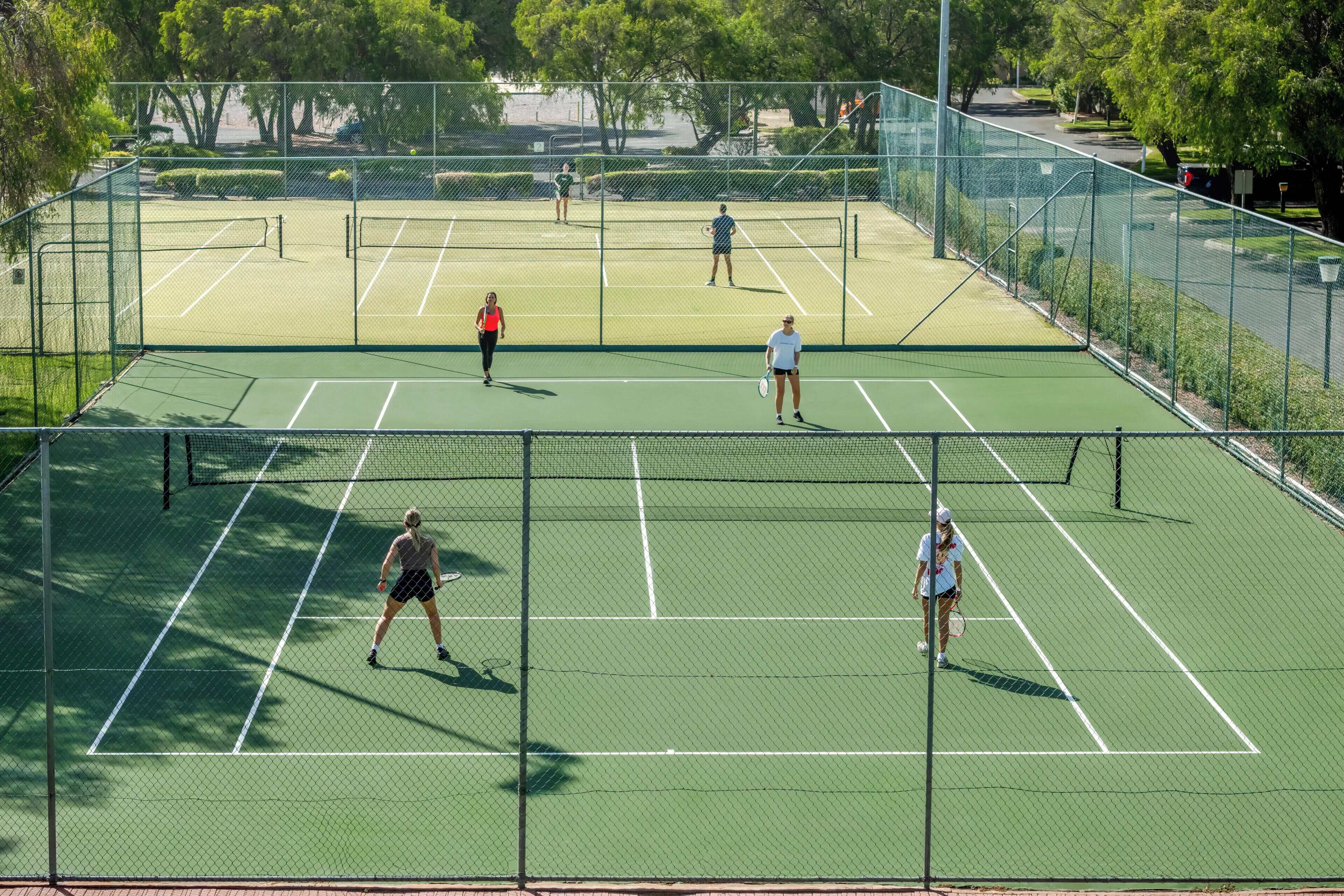 A tennis court with four players, surrounded by a fence and trees.