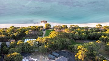 Vista aérea de una zona costera con playa, árboles y un estacionamiento.