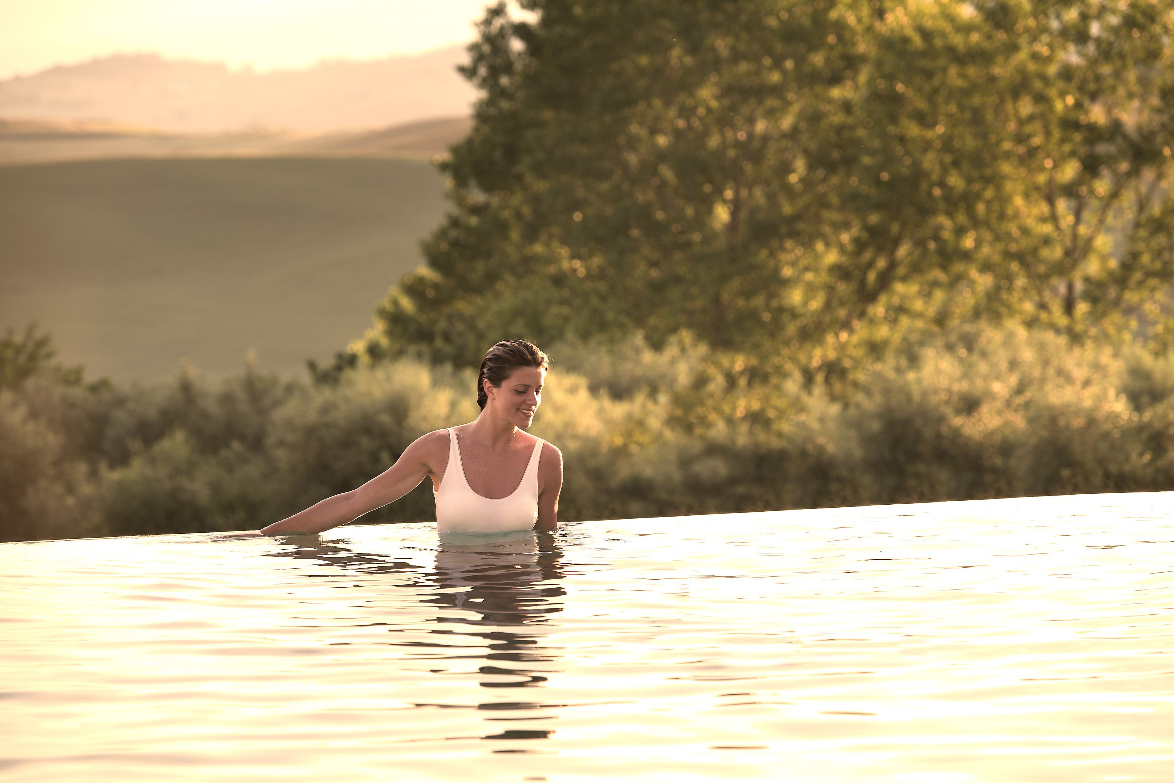 A person in a swimming pool with a natural landscape in the background.