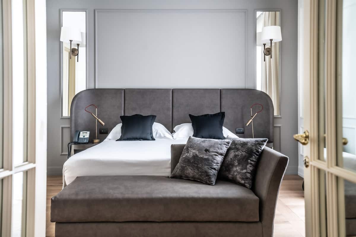 A modern bedroom with a large bed, two bedside tables, a nightstand, and a grey upholstered bench.