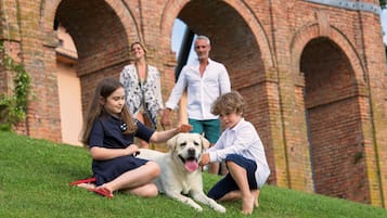 Una familia interactúa con un perro en una pendiente cubierta de hierba, con un arco de ladrillo al fondo.
