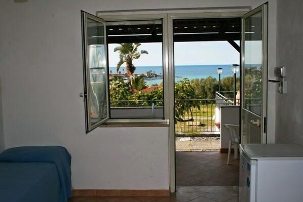 A room with a sliding glass door leading to a balcony with a view of the sea and palm trees. - Villaggio Dolomiti sul Mare (Briatico)