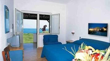 Una stanza con un letto, una poltrona blu, una televisione e una finestra vista mare.