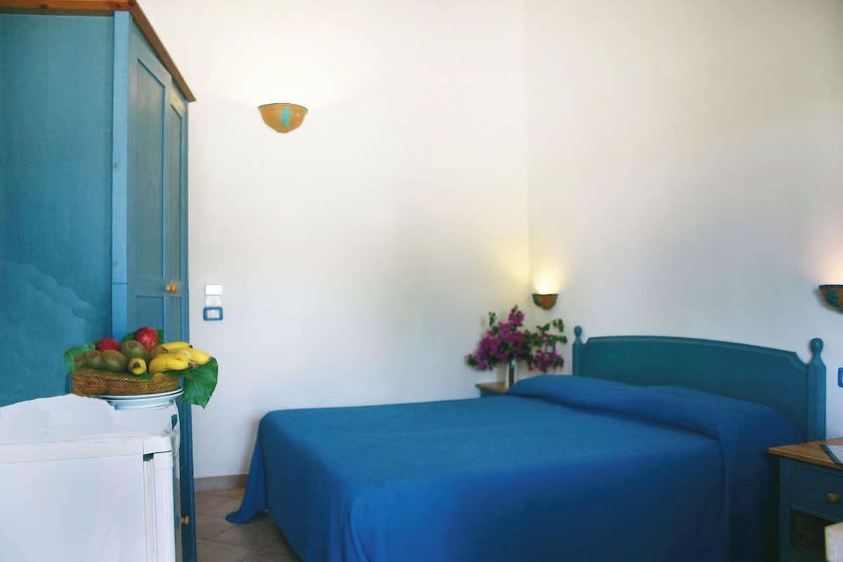 Een kamer met een bed, nachtkastje, lamp en een fruitmand op een tafel.
