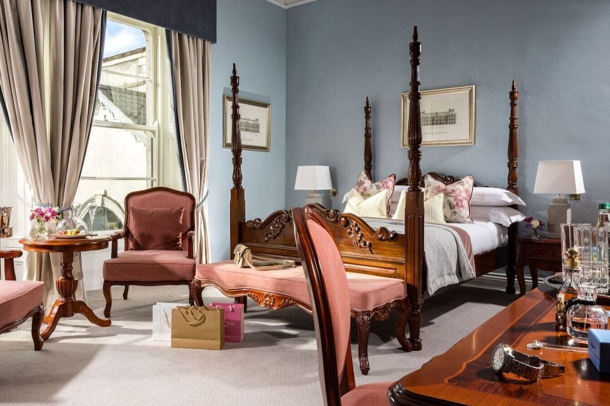 Habitación de hotel con cama con dosel, zona de estar con mesa y sillas, y vista al exterior.
