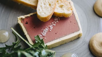 A slice of meat terrine on a plate with a slice of bread and some greens.