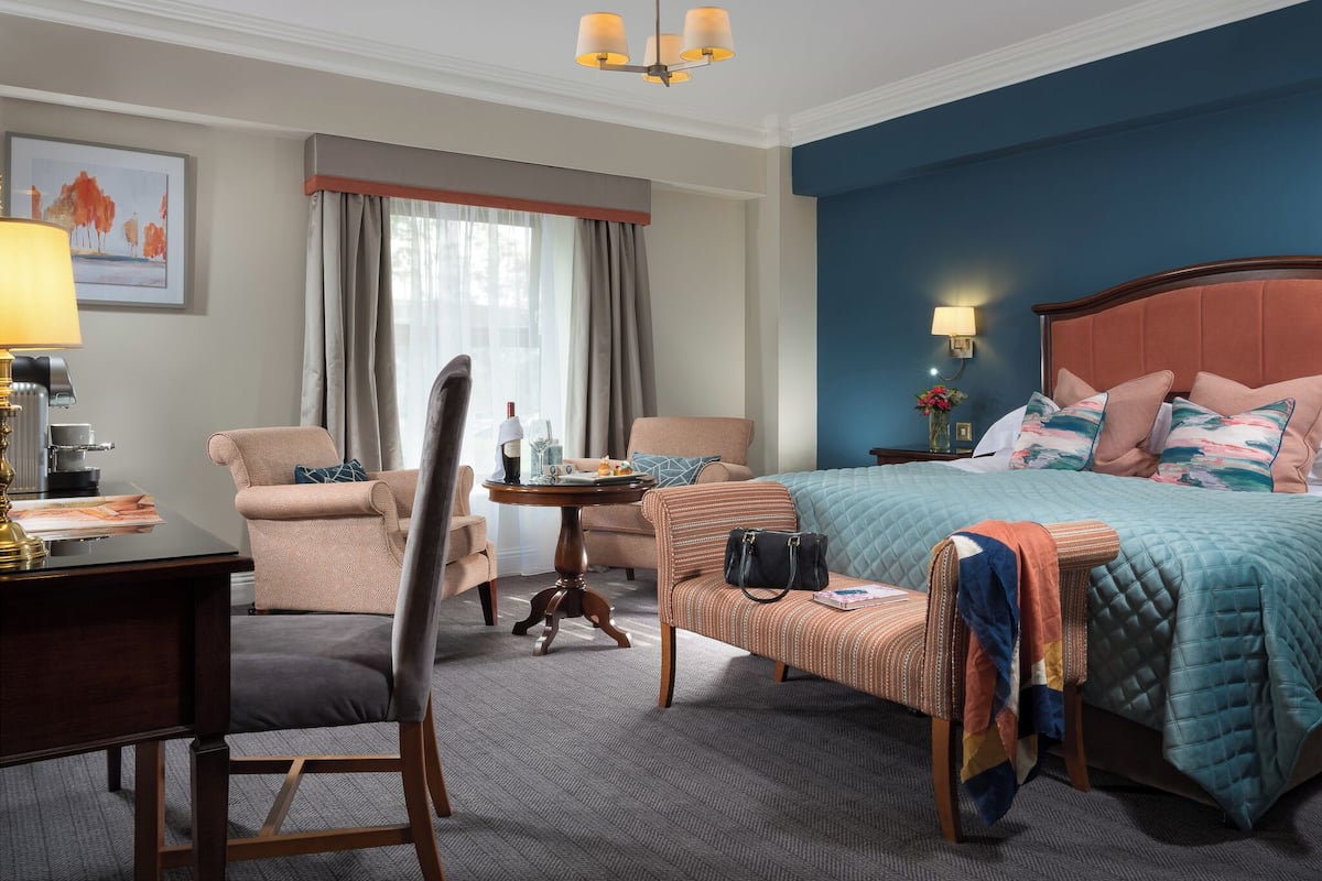 Una habitación de hotel con cama, escritorio, silla, mesita y ventana con cortinas.