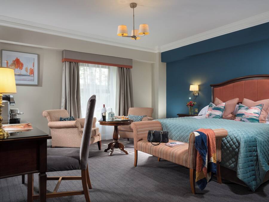 Ein Hotelzimmer mit Bett, Schreibtisch, Stuhl, kleinem Tisch und einem Fenster mit Vorhängen.