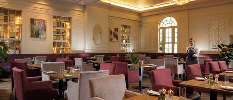 A spacious restaurant with high ceilings, elegant chandeliers, and a variety of seating arrangements including booths and tables.