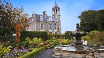 A historic building with a tower, surrounded by a well-maintained garden with a central fountain.
