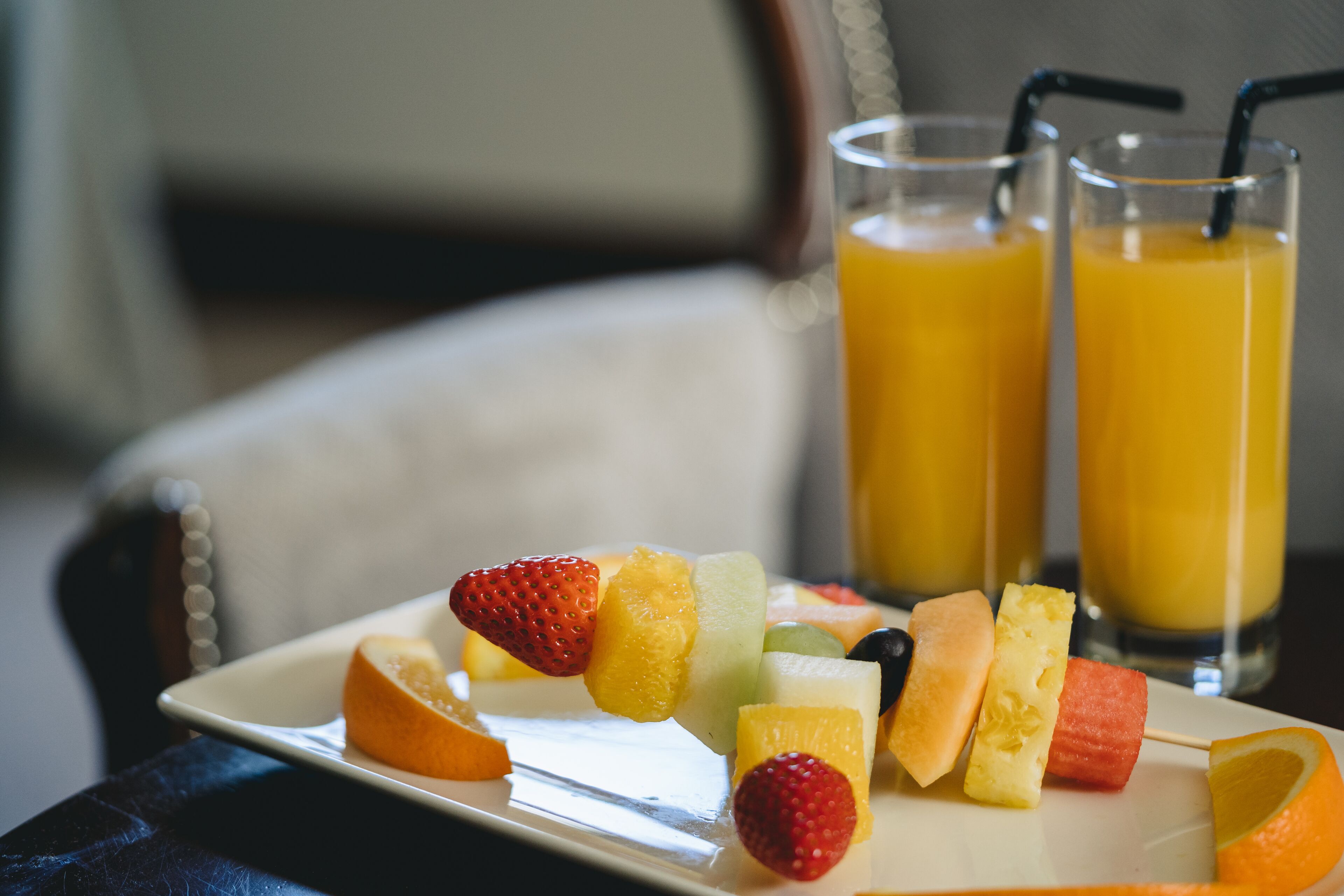 A plate of fruit skewers and two glasses of orange juice.