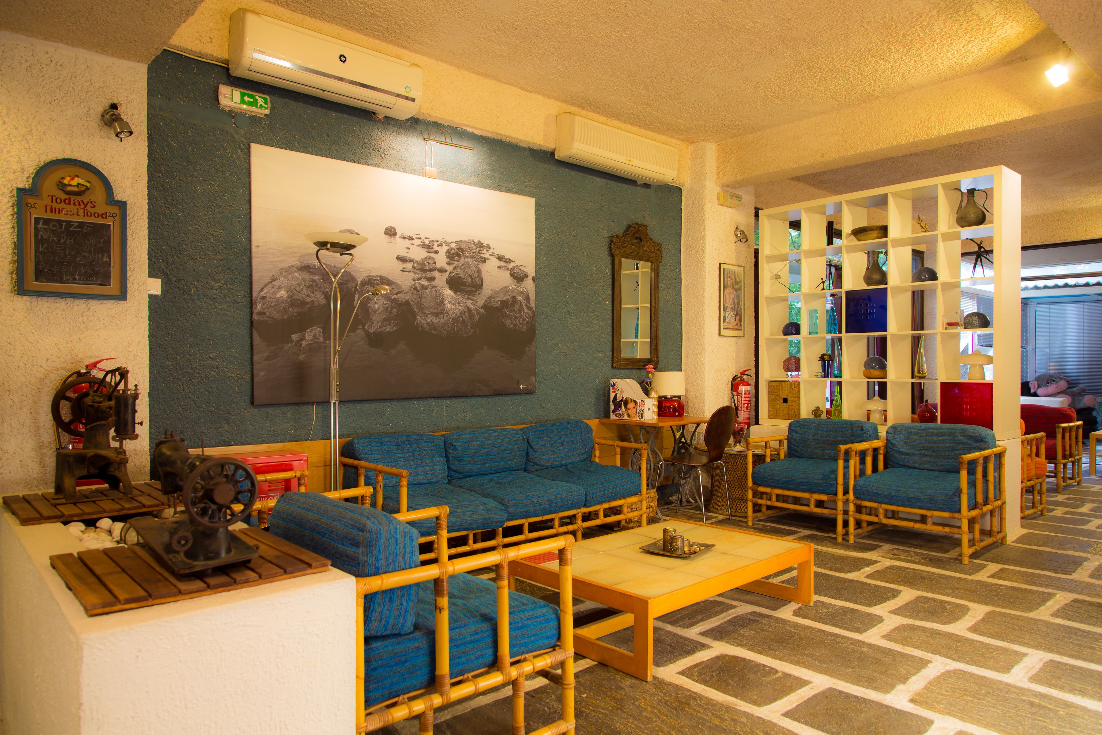 Una habitación con un sofá azul, dos sillones, una mesa de centro de madera y una estantería con varios objetos.