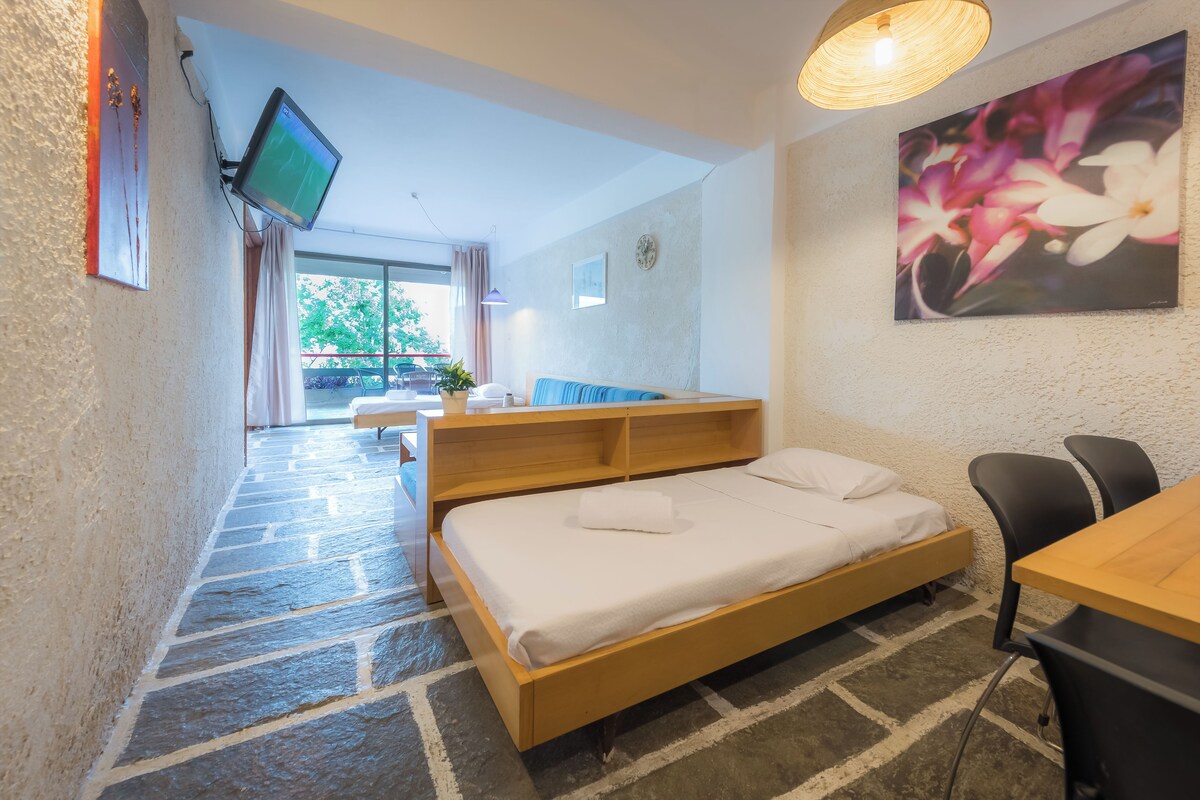 A bedroom with a bed, a desk, a chair, a TV, and a painting.