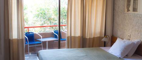 Une chambre d’hôtel avec un lit, une chaise, une table et une vue sur la verdure.