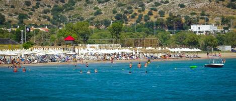 A beach with people swimming and sunbathing, umbrellas, and a boat.