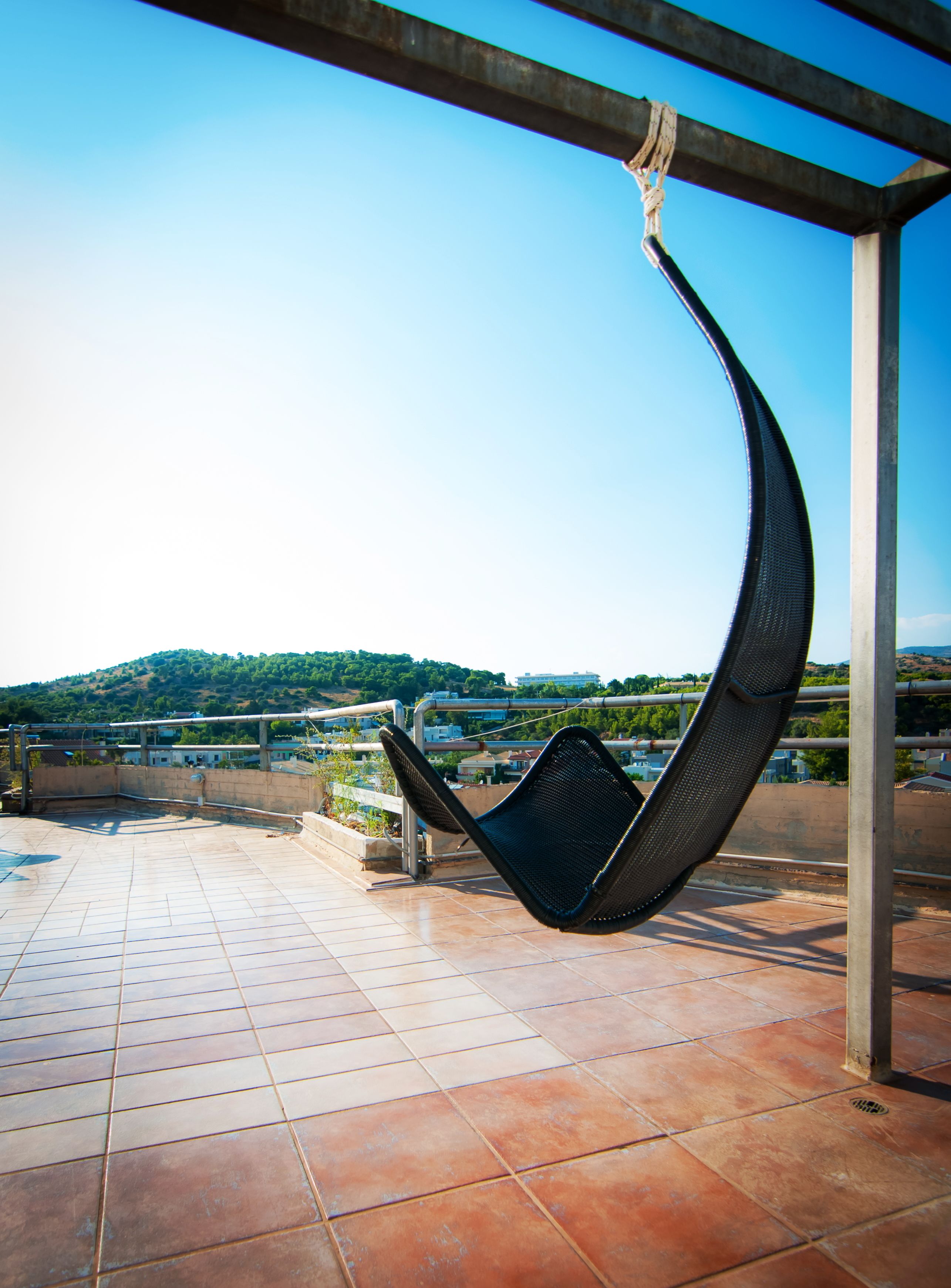 A hammock chair on a tiled patio with a view of a hilly landscape.