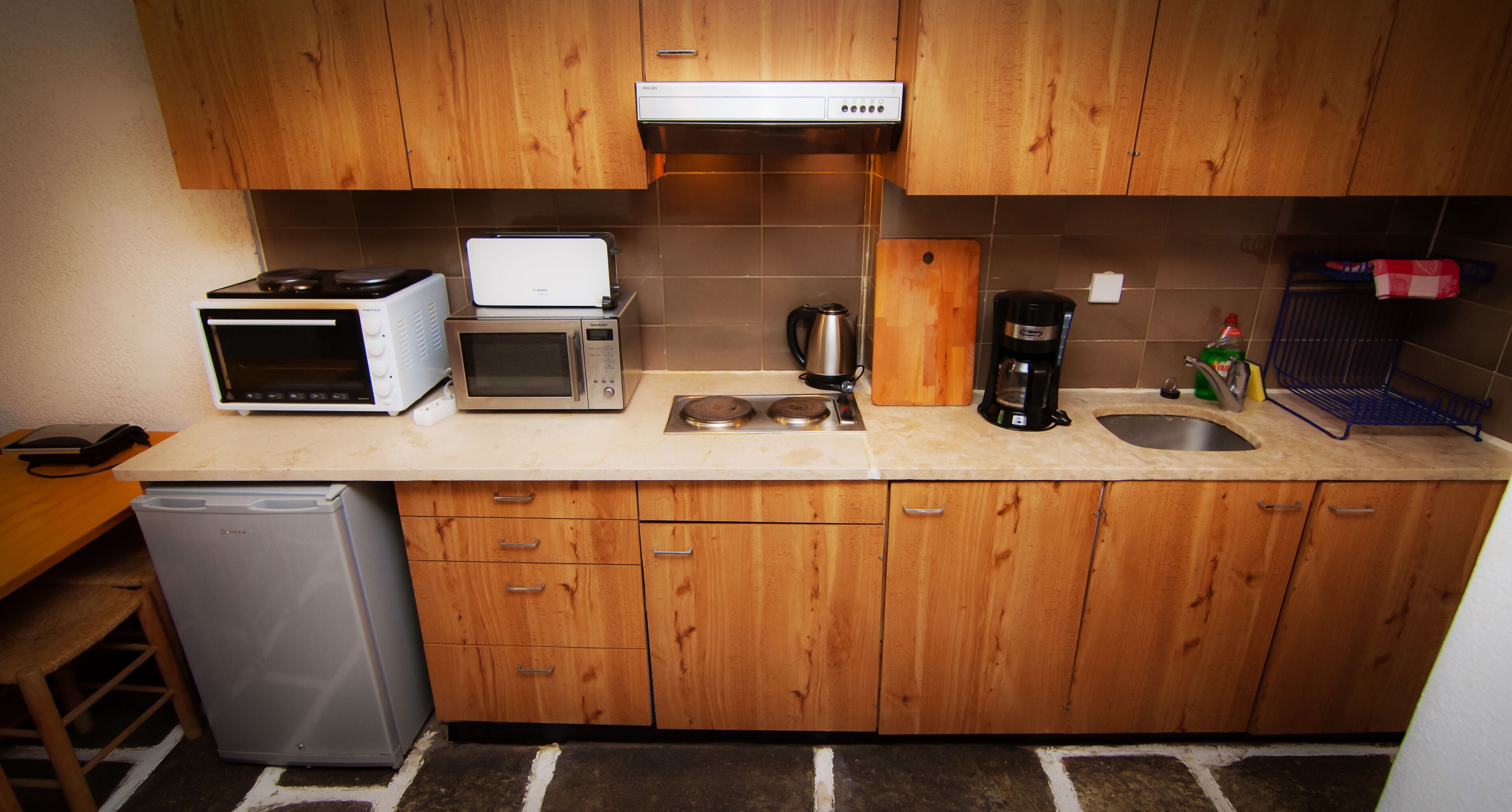 Cocina compacta con armarios de madera, microondas, cafetera y lavavajillas.