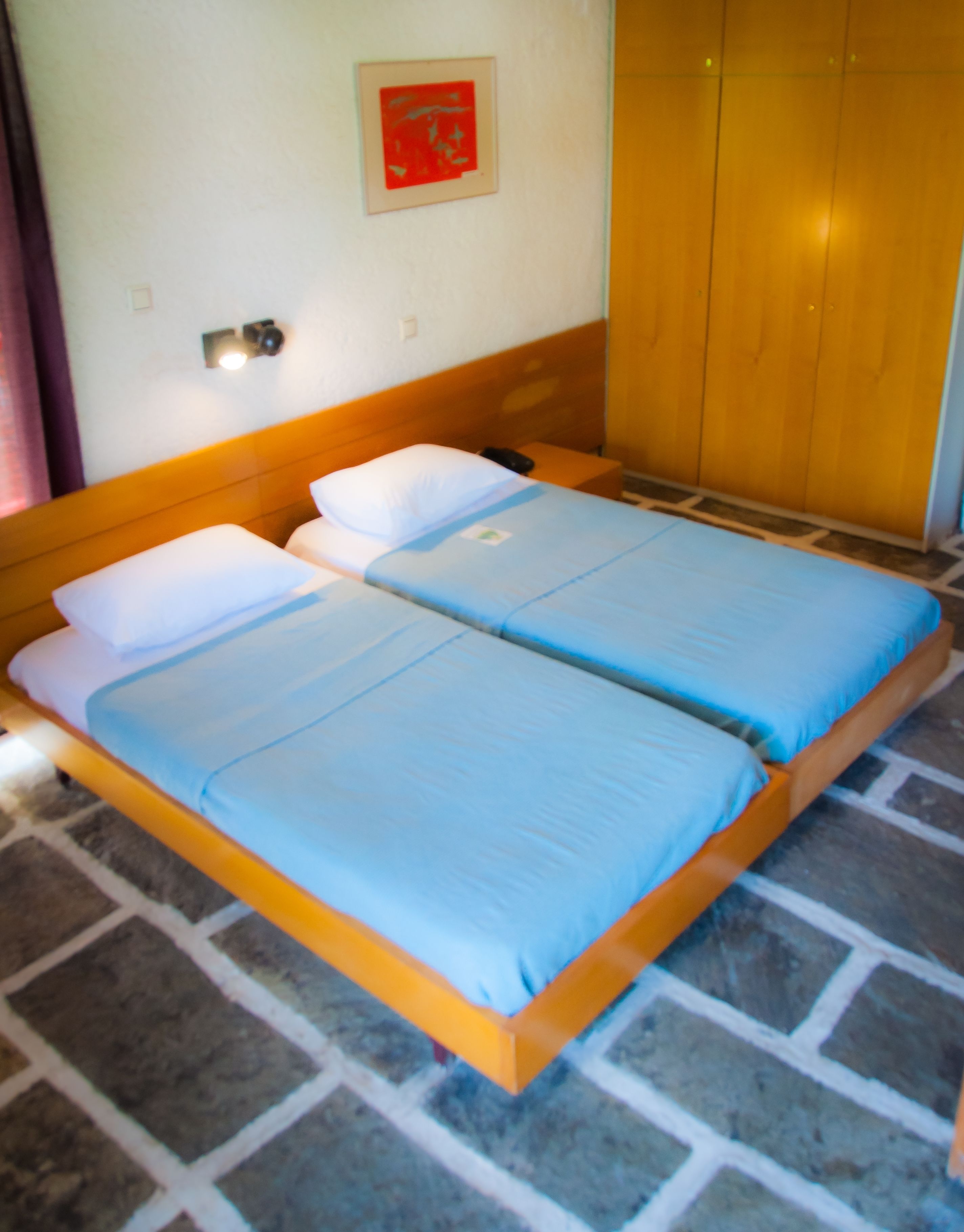 Un lit double avec une literie bleue, une tête de lit en bois et un sol carrelé.