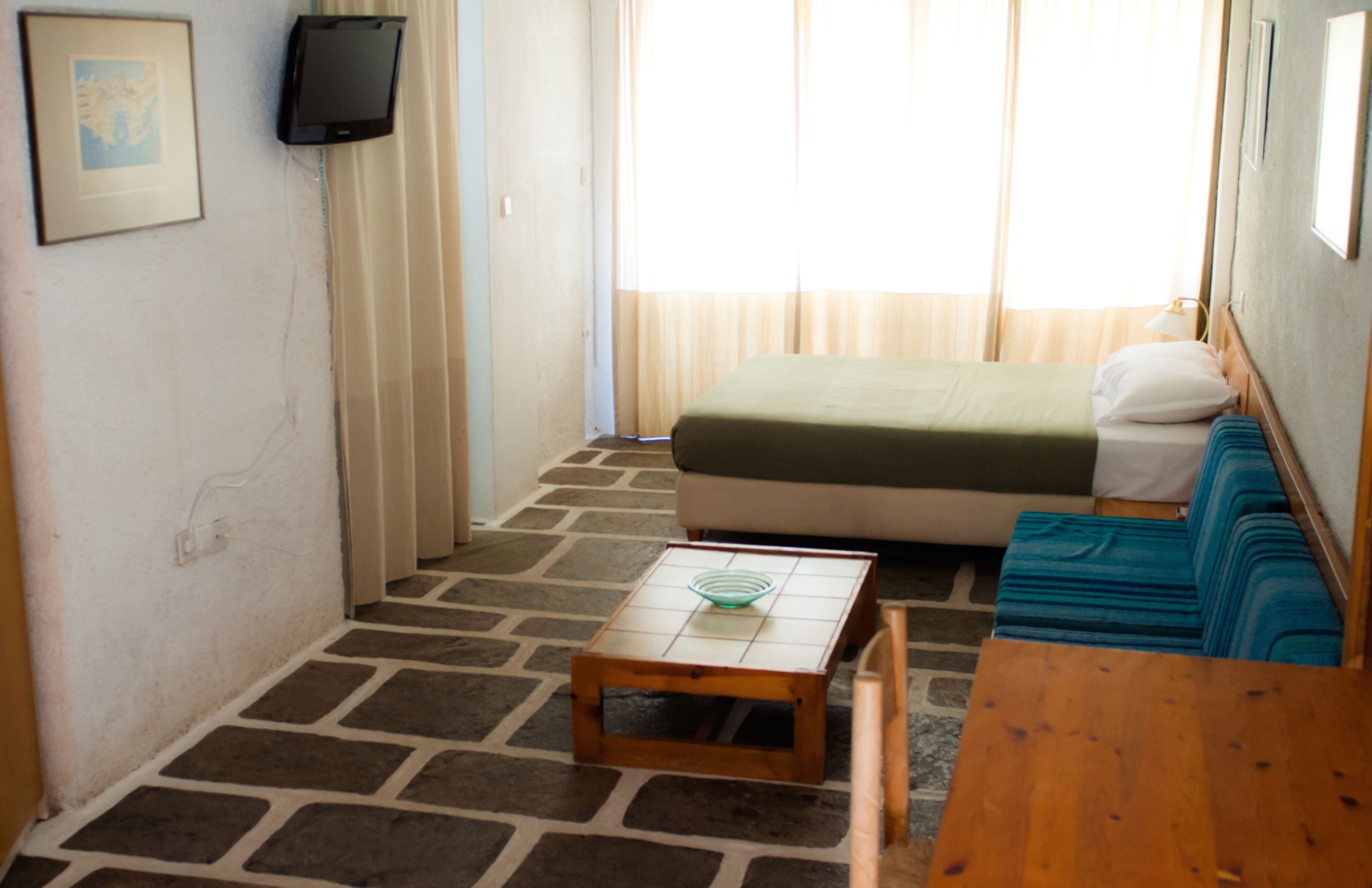 A small, cozy room with a bed, a wooden table, and a blue sofa.