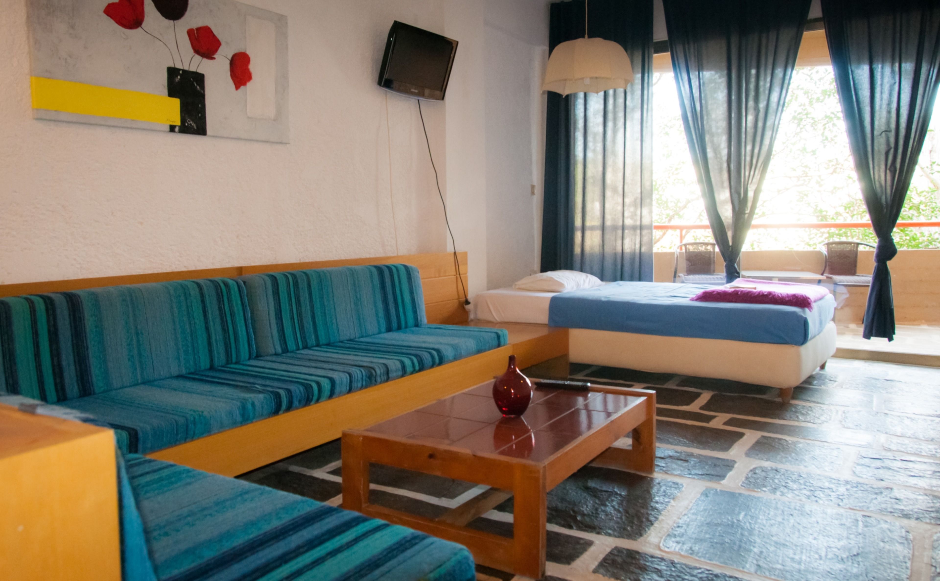 A room with a sofa, a bed, a small table, and a TV on the wall.