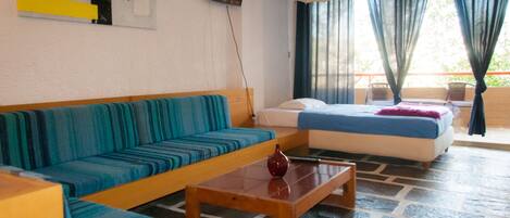 A room with a sofa, a bed, a small table, and a TV on the wall.