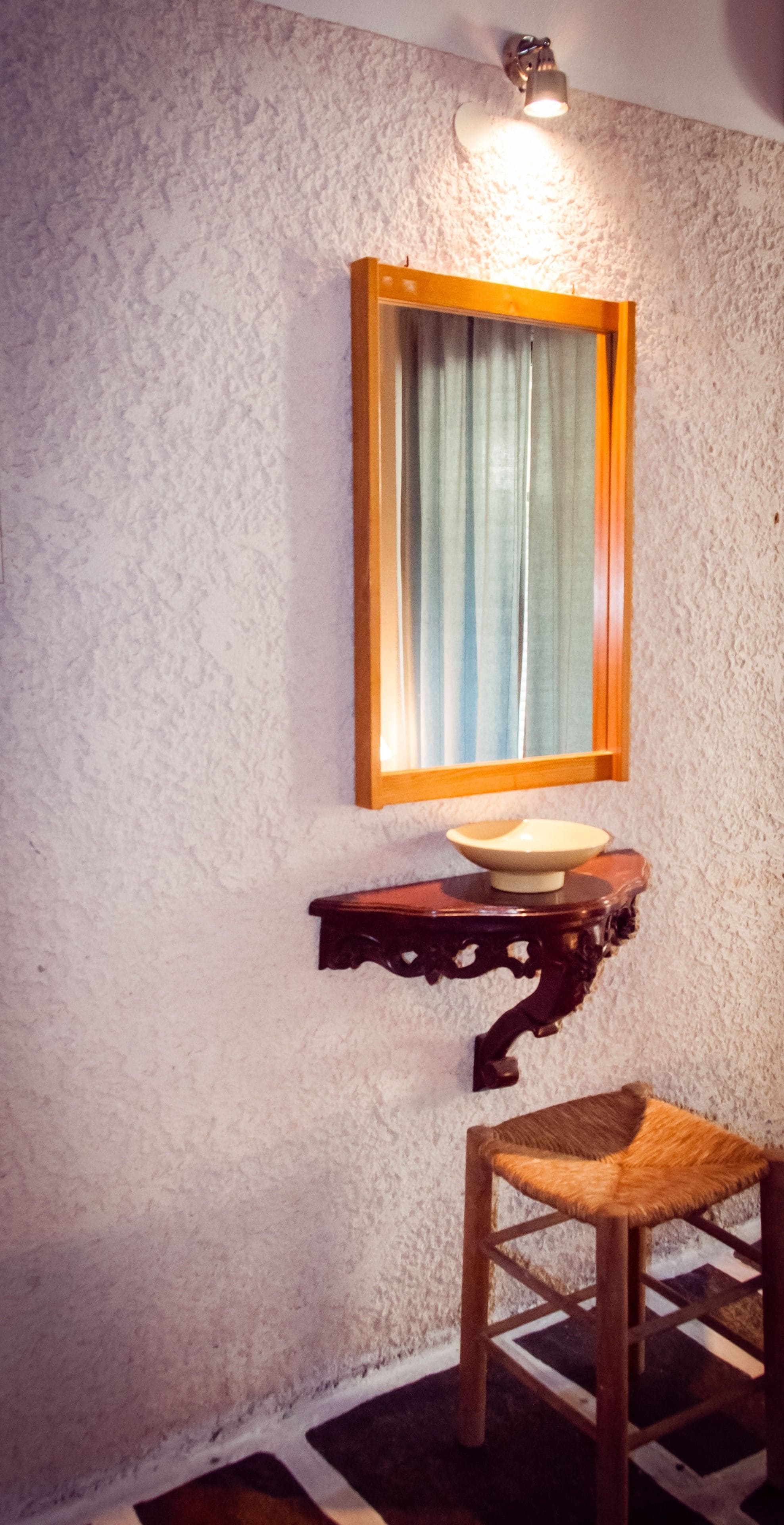 A bathroom with a textured wall, a wooden medicine cabinet, a round mirror, and a wooden chair.