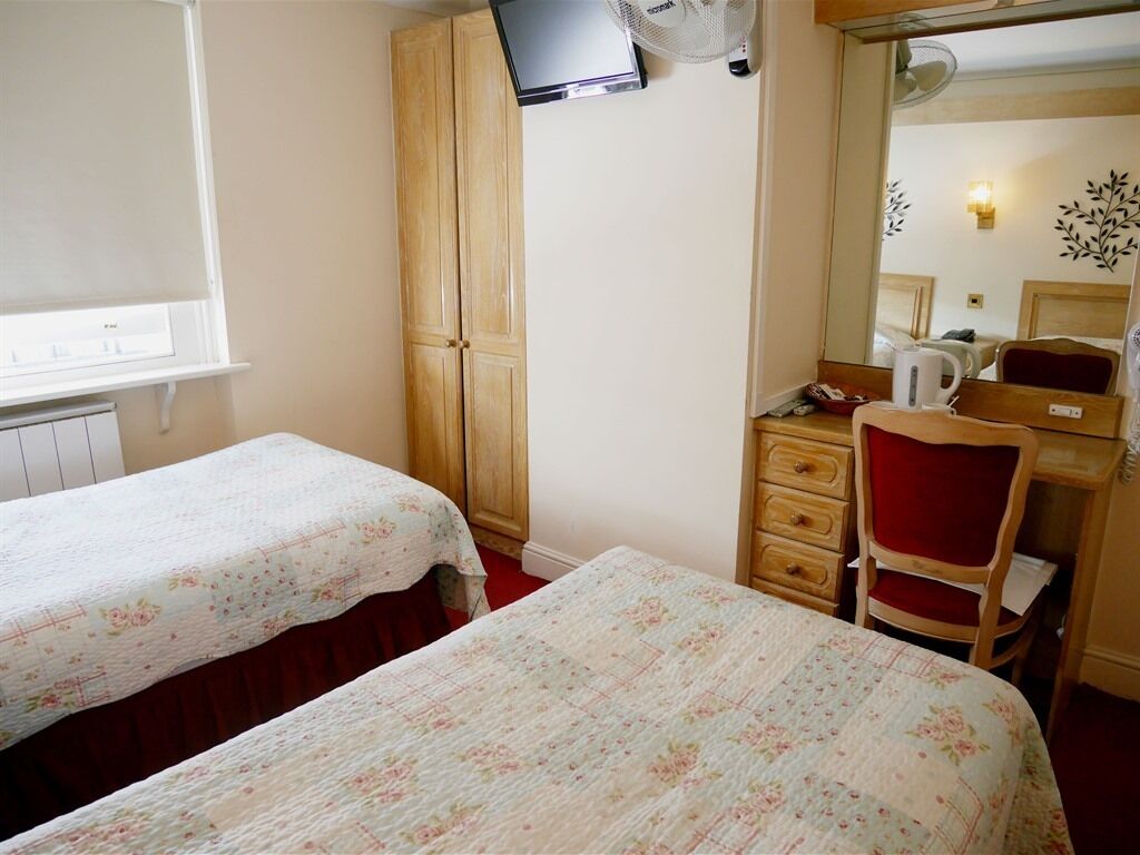 A bedroom with two beds, a wooden wardrobe, a desk with a chair, and a mirror.
