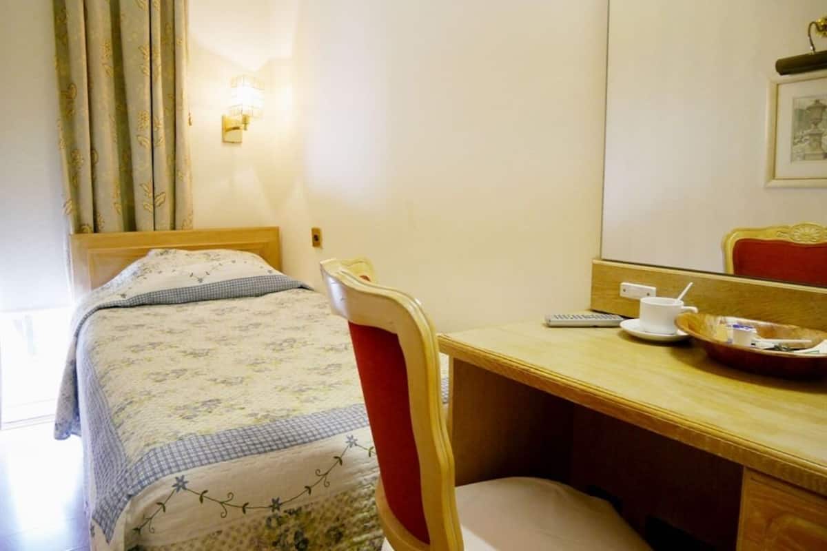 Una habitación de hotel con cama, escritorio, silla, mesita de noche, lámpara y espejo.
