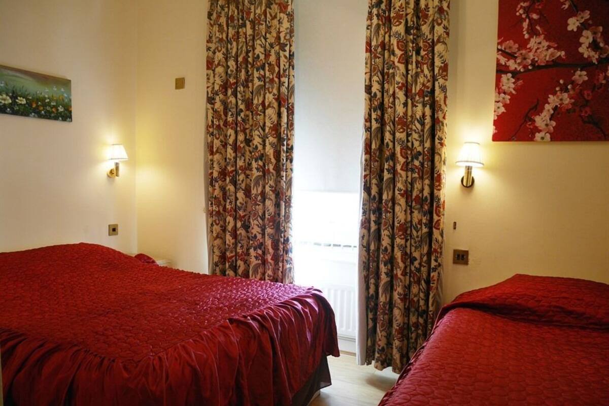 Una habitación de hotel con dos camas, cortinas florales, lámparas de pared y un cuadro.