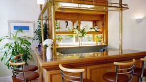 Un espace bar doté de tabourets de bar en bois, d’un comptoir de bar avec un plateau en verre et d’un miroir au-dessus du comptoir.