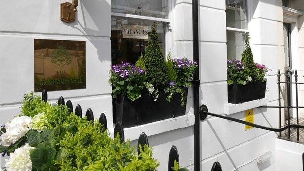 La façade d’un hôtel, avec une enseigne indiquant les chambres disponibles, un lampadaire traditionnel et des jardinières sur les rebords des fenêtres.