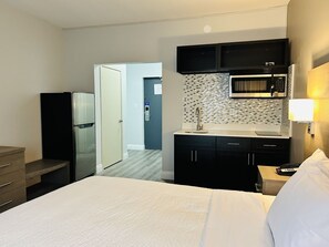 A hotel room with a bed, a minibar, a microwave, a sink, and a door leading to a bathroom. - Motel 6 Sault Ste. Marie, ON (Sault Ste. Marie)