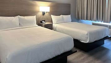 A hotel room with two beds, a nightstand with a phone, a wall-mounted lamp, and a window with curtains.