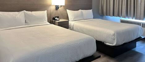 A hotel room with two beds, a nightstand with a phone, a wall-mounted lamp, and a window with curtains.