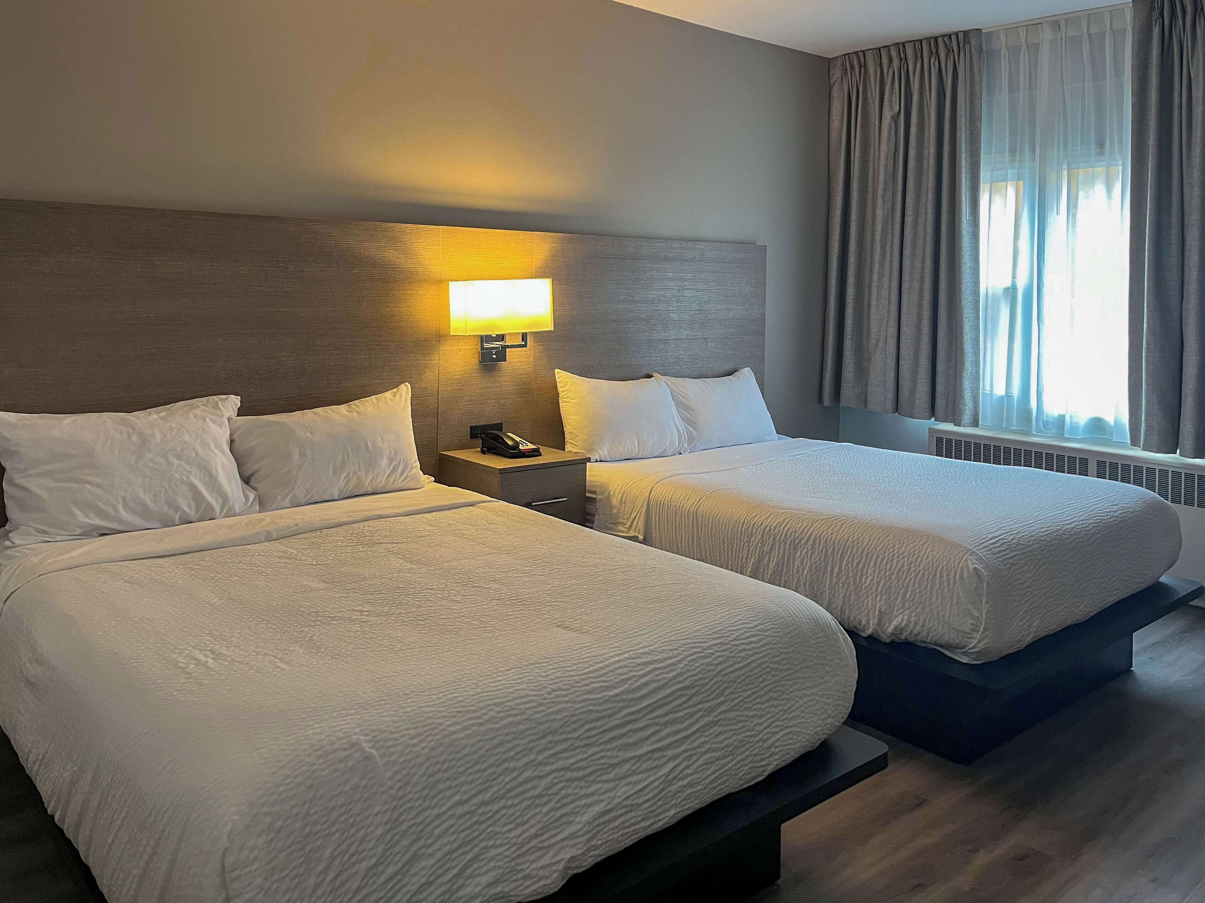 Habitación de hotel con dos camas, una mesita de noche con lámpara, teléfono y ventana con cortinas.