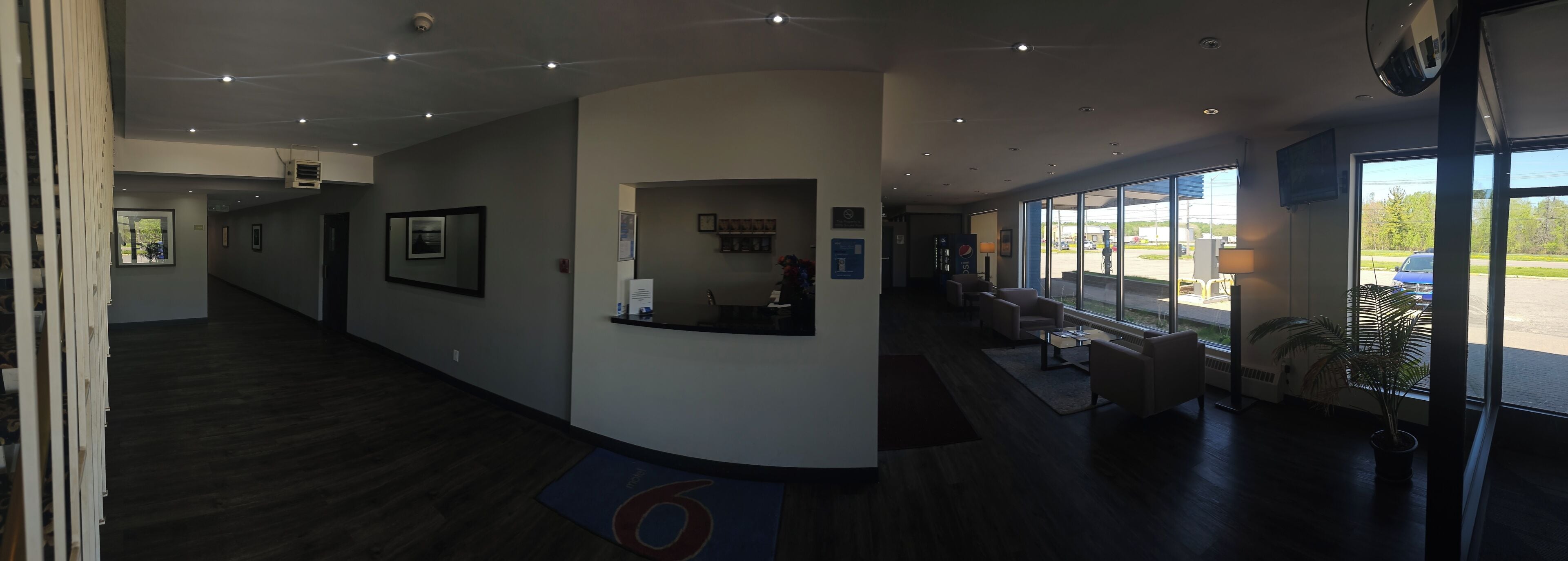 A hotel lobby with a reception desk, seating area, and large windows offering a view of the parking lot.