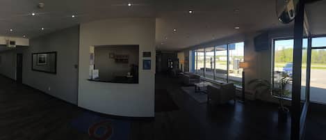 A hotel lobby with a reception desk, seating area, and large windows offering a view of the parking lot.