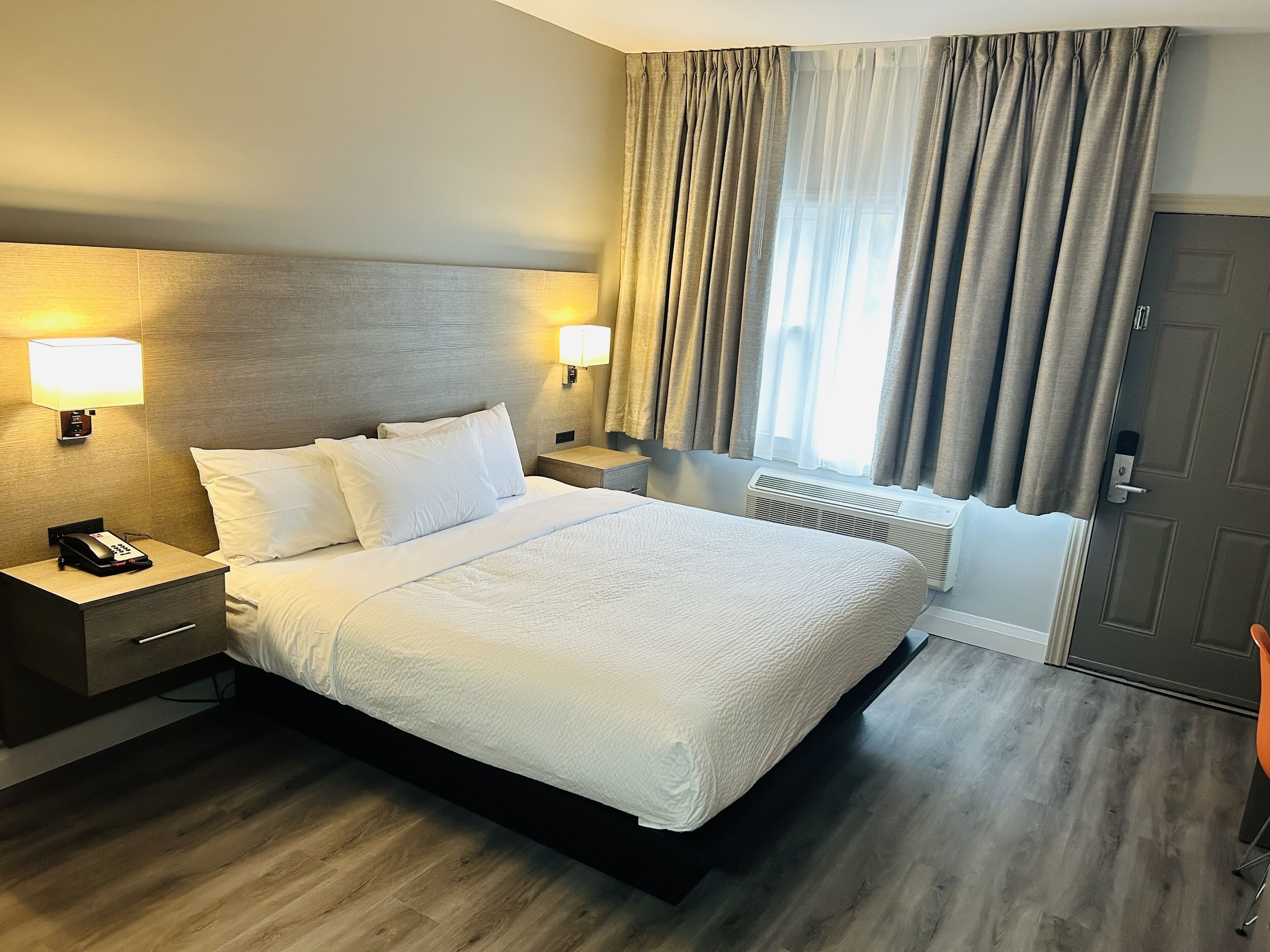 Ein Hotelzimmer mit einem großen Bett, zwei Nachttischlampen, einem Telefon, einem Nachttisch, einem Heizkörper und einer Tür.