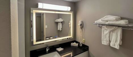 A bathroom with a large mirror, a black countertop, a white sink, a towel rack, and a toilet.
