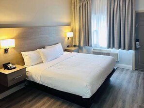 A hotel room with a large bed, two bedside tables with lamps, a heater, and a door. - Motel 6 Sault Ste. Marie, ON (Sault Ste. Marie)