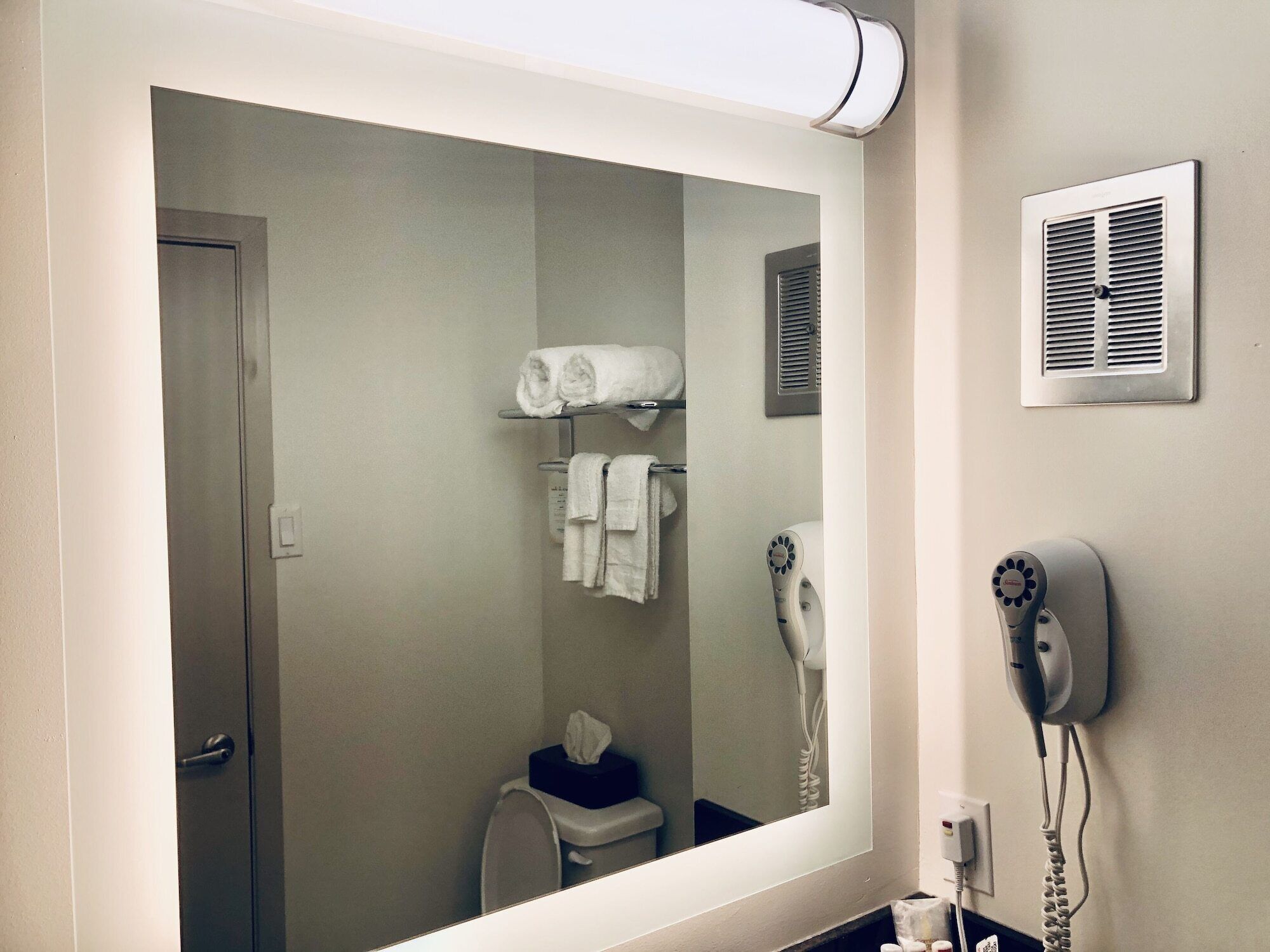 A bathroom with a large mirror, a hairdryer, and a towel rack with towels.