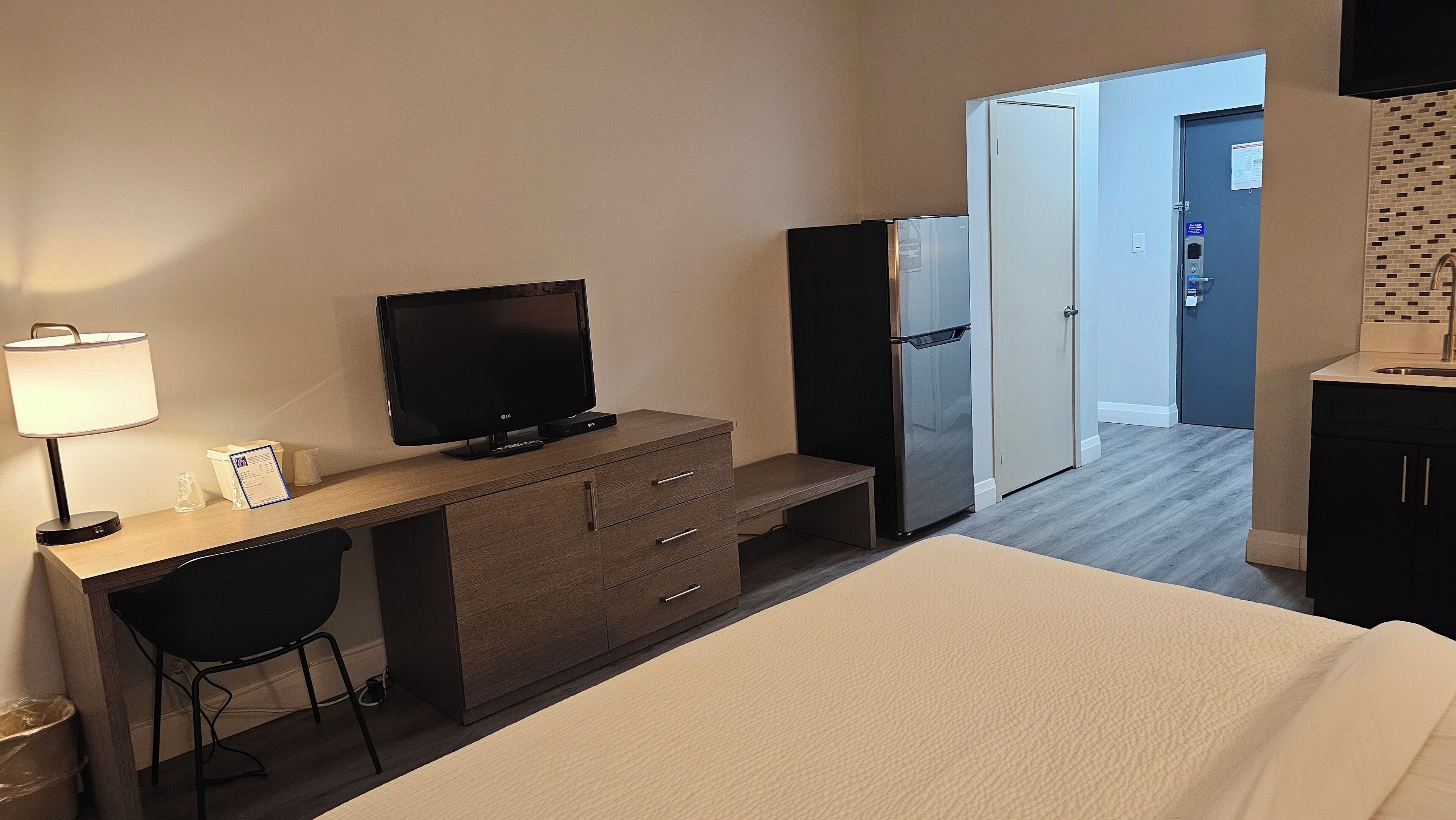 Una camera d'albergo con un letto, una scrivania con la TV, un frigorifero e angolo cottura.