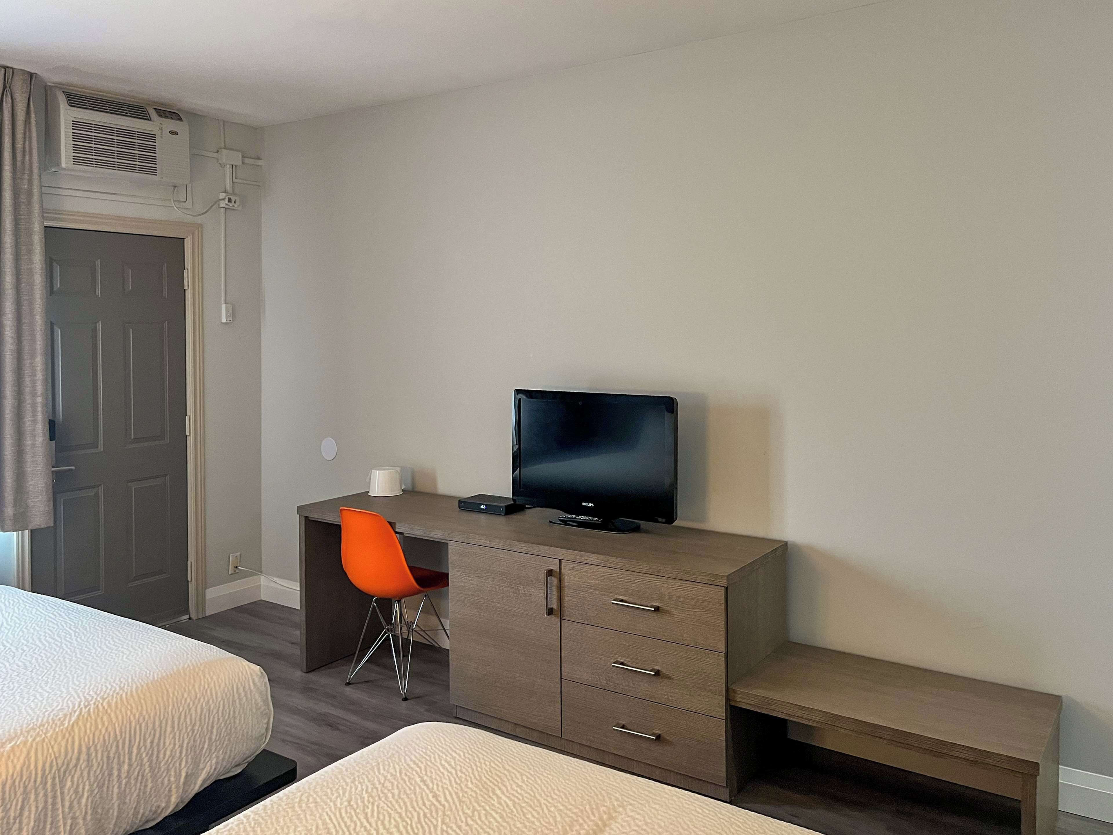 Une chambre d’hôtel avec un lit, un bureau avec une télévision, une chaise et une petite table.