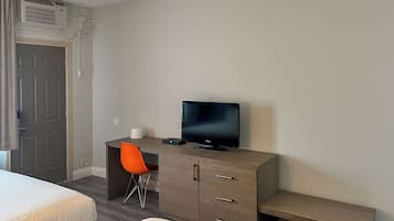 Une chambre d’hôtel avec un lit, un bureau avec une télévision, une chaise et une petite table.
