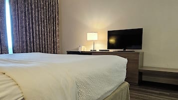 A hotel room with a large bed, a flat-screen TV, a bedside table with a lamp, and a wooden bench.