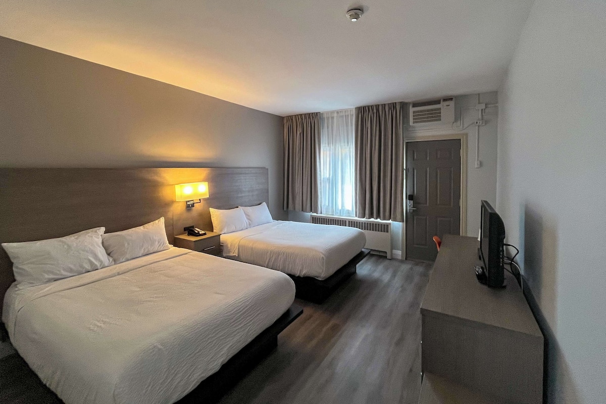 Une chambre d’hôtel avec deux lits, une table de chevet avec une lampe, une télévision et une fenêtre avec des rideaux.